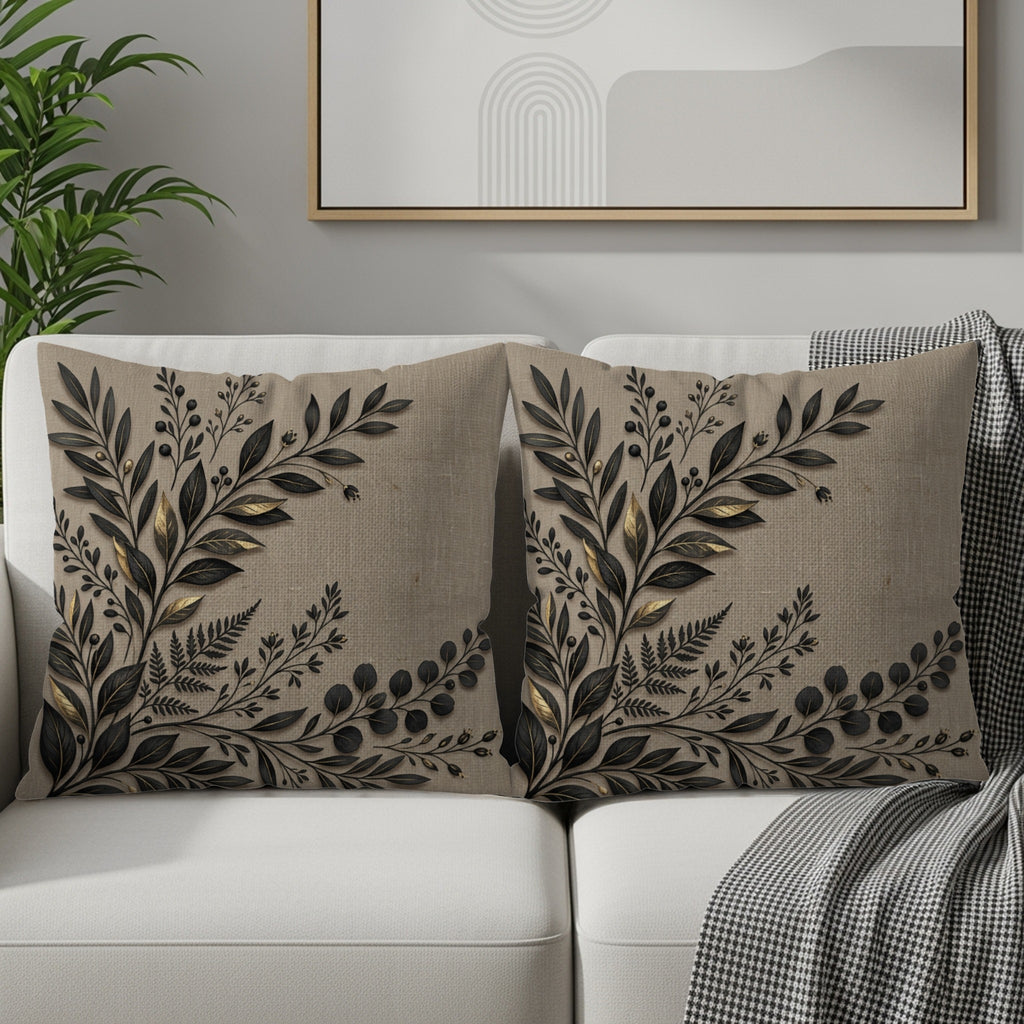 Two linen throw pillows with black botanical leaf embroidery on a sofa.