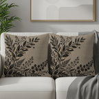 Two linen throw pillows with black botanical leaf embroidery on a sofa.