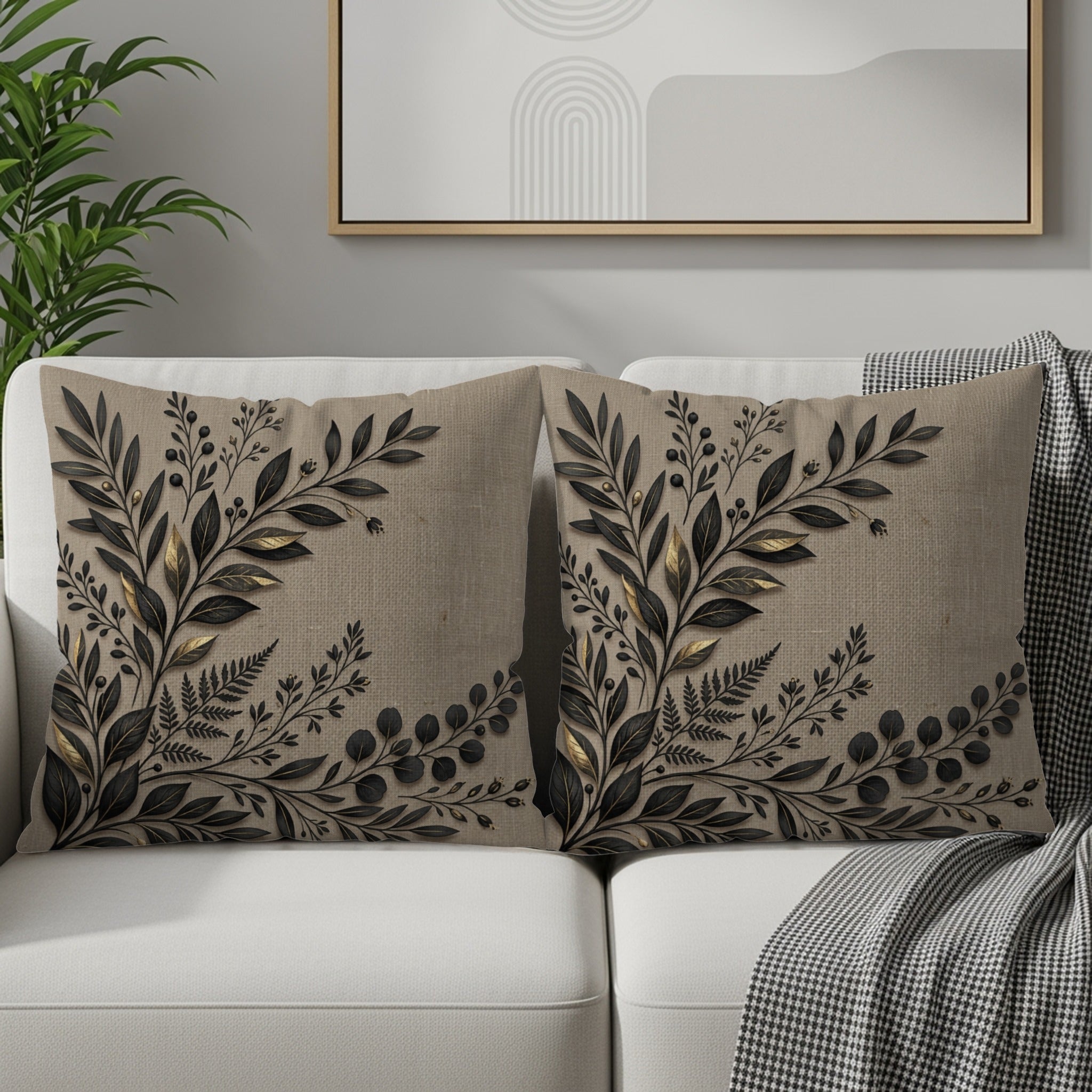 Two linen throw pillows with black botanical leaf embroidery on a sofa.