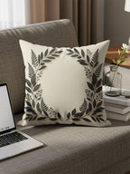 Cream throw pillow with dark floral wreath design on a sofa.