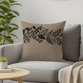 Beige pillow with black floral branch design on gray couch.