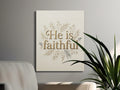 "He is faithful" text with floral border on canvas art, displayed above a couch.
