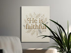 "He is faithful" text with floral border on canvas art, displayed above a couch.
