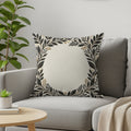 Cream throw pillow with a black and gold floral border on a gray sofa.