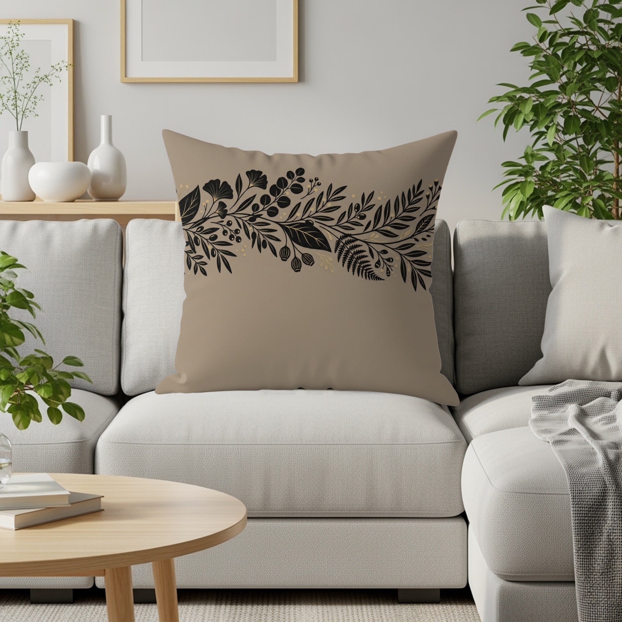 Tan throw pillow with black floral and leaf border design on a couch.