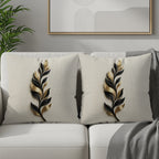 Two cream throw pillows with black and gold feather designs on a white sofa.