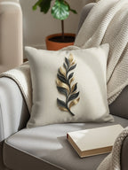 Cream pillow with a gold and black metallic leaf design on a grey armchair.