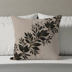 Beige pillow with raised black and gold leaf design on white pillows and bed.