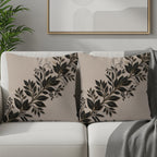 Two decorative throw pillows with a black leaf and vine pattern on a beige background.