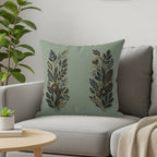 Sage green throw pillow with two symmetrical gold and dark green floral designs.