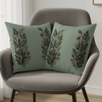 Two sage green decorative pillows with gold and black floral designs on a chair.