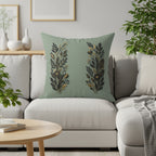Sage green pillow with gold floral design on a sofa.