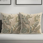 Two square throw pillows with a muted green and beige floral leaf pattern.