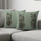 Sage green throw pillows with gold and black floral patterns on a couch.