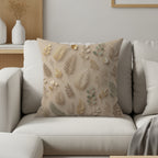 Beige throw pillow with repeating pattern of muted gold and sage green botanical illustrations.