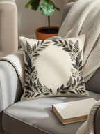 Cream throw pillow with dark botanical wreath design on armchair.