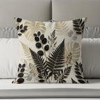 Square pillow with black and gold fern and leaf pattern on a bed.
