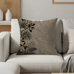 Tan throw pillow with a black and gold tropical leaf pattern.
