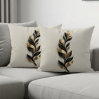 Two decorative throw pillows with gold and black leaf pattern on a sofa.
