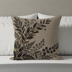 Tan throw pillow with dark botanical embroidery in corner on a bed.