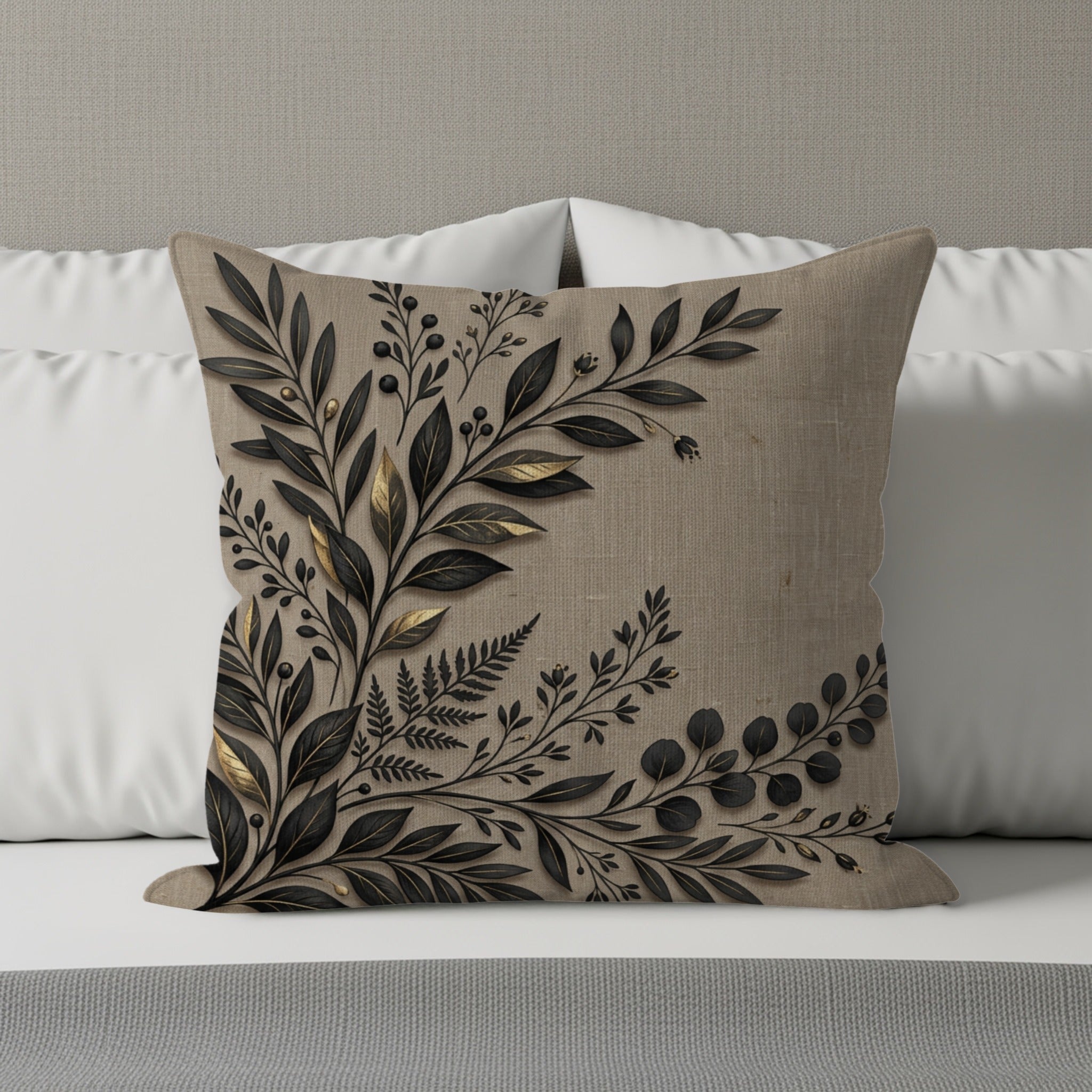 Tan throw pillow with dark botanical embroidery in corner on a bed.