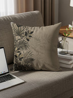 Tan throw pillow with dark botanical pattern on a sofa next to a laptop.