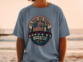 Blue t-shirt with "In God We Trust" emblem featuring American flag, cross, and dates.