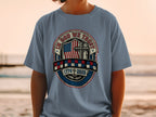 Blue t-shirt with "In God We Trust" emblem featuring American flag, cross, and dates.