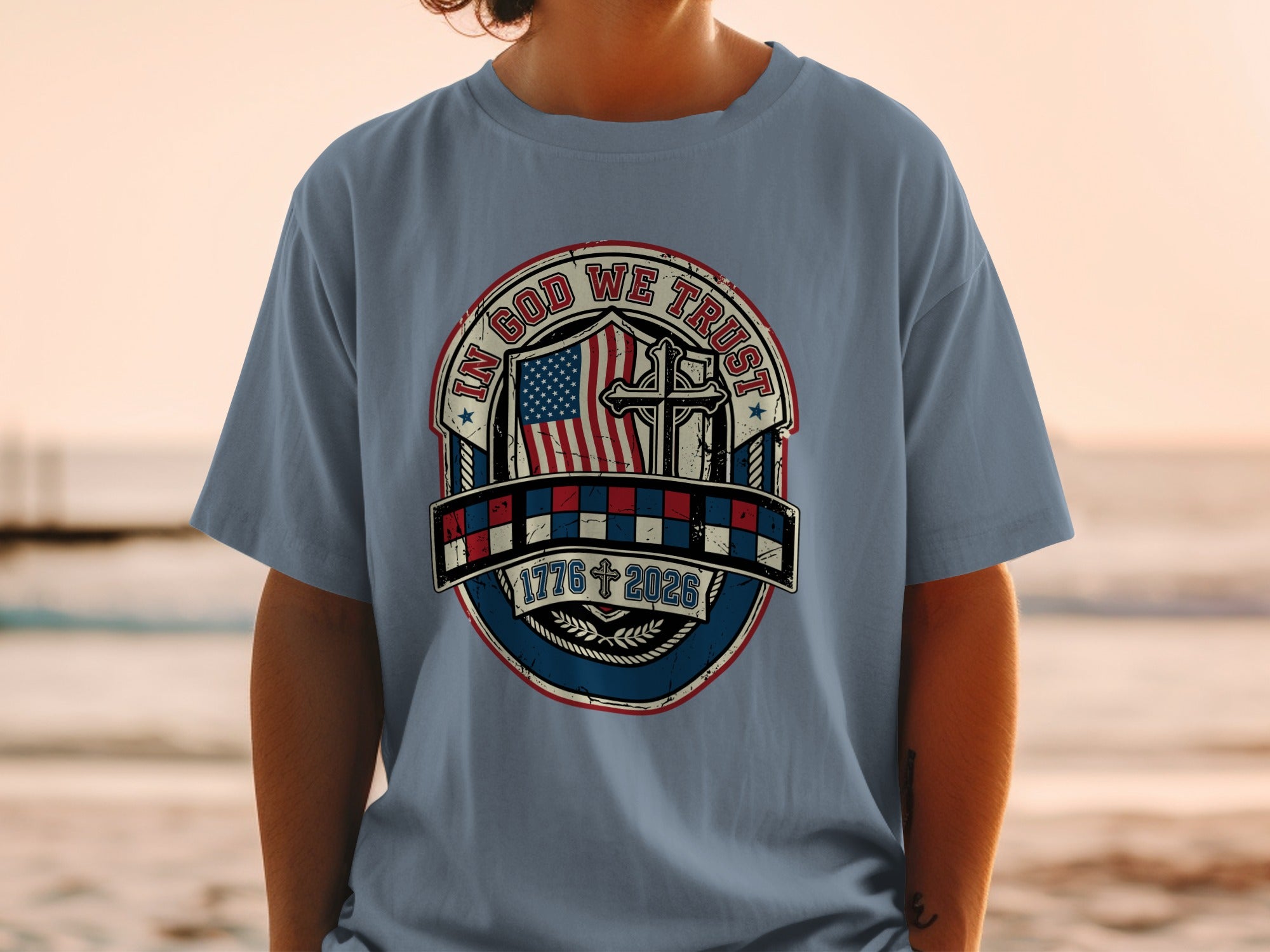 Blue t-shirt with "In God We Trust" emblem featuring American flag, cross, and dates.