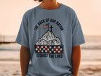 T-shirt with American flag on mountain, checkered band, and "The Rock of Our Nation Is Christ the Lord" text.