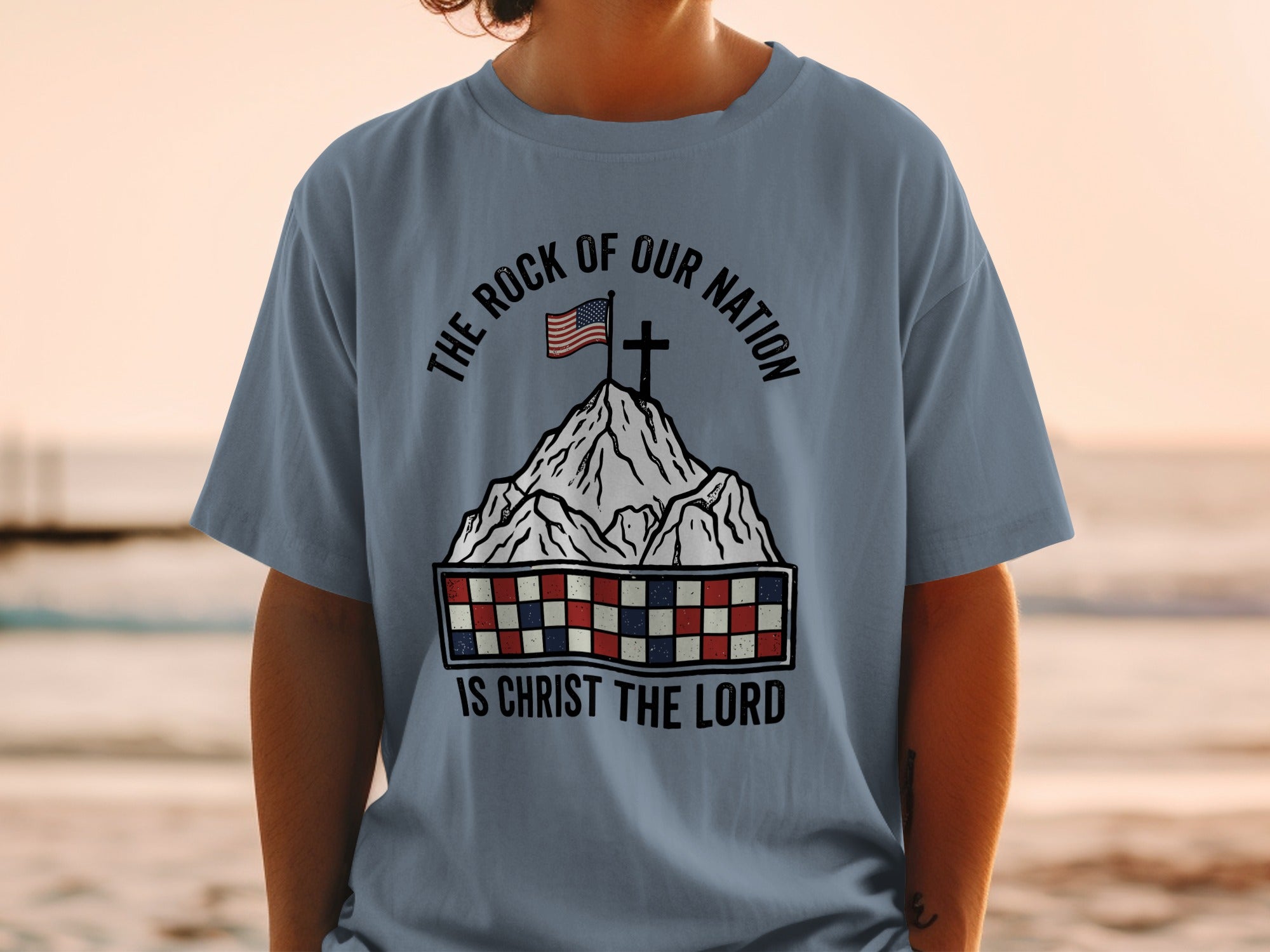 T-shirt with American flag on mountain, checkered band, and "The Rock of Our Nation Is Christ the Lord" text.