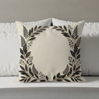 Cream square pillow with a black floral wreath design on a bed.