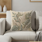 Beige throw pillow with abstract green and beige leaf pattern on white sofa.