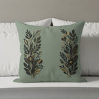 Sage green throw pillow with gold and black floral design on a bed.
