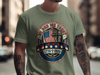 Green t-shirt with patriotic shield featuring flag, cross, and dates 1776-2026.