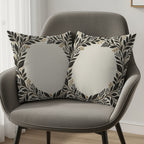 Two throw pillows with cream centers and black and gold floral borders on a gray chair.