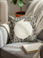Throw pillow with botanical leaf wreath on armchair with blanket and book.